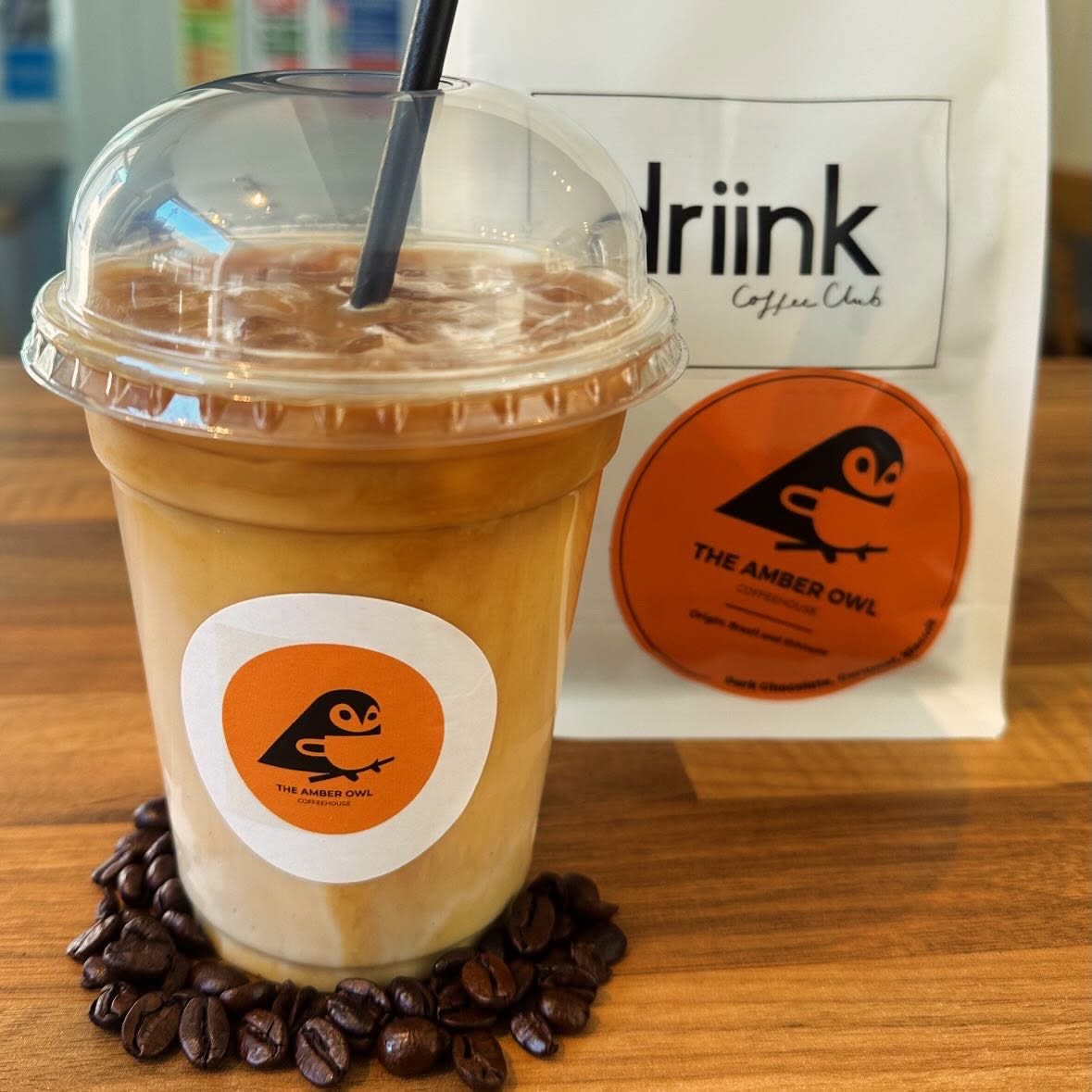 Iced oat milk latte beside a bag of house coffee beans