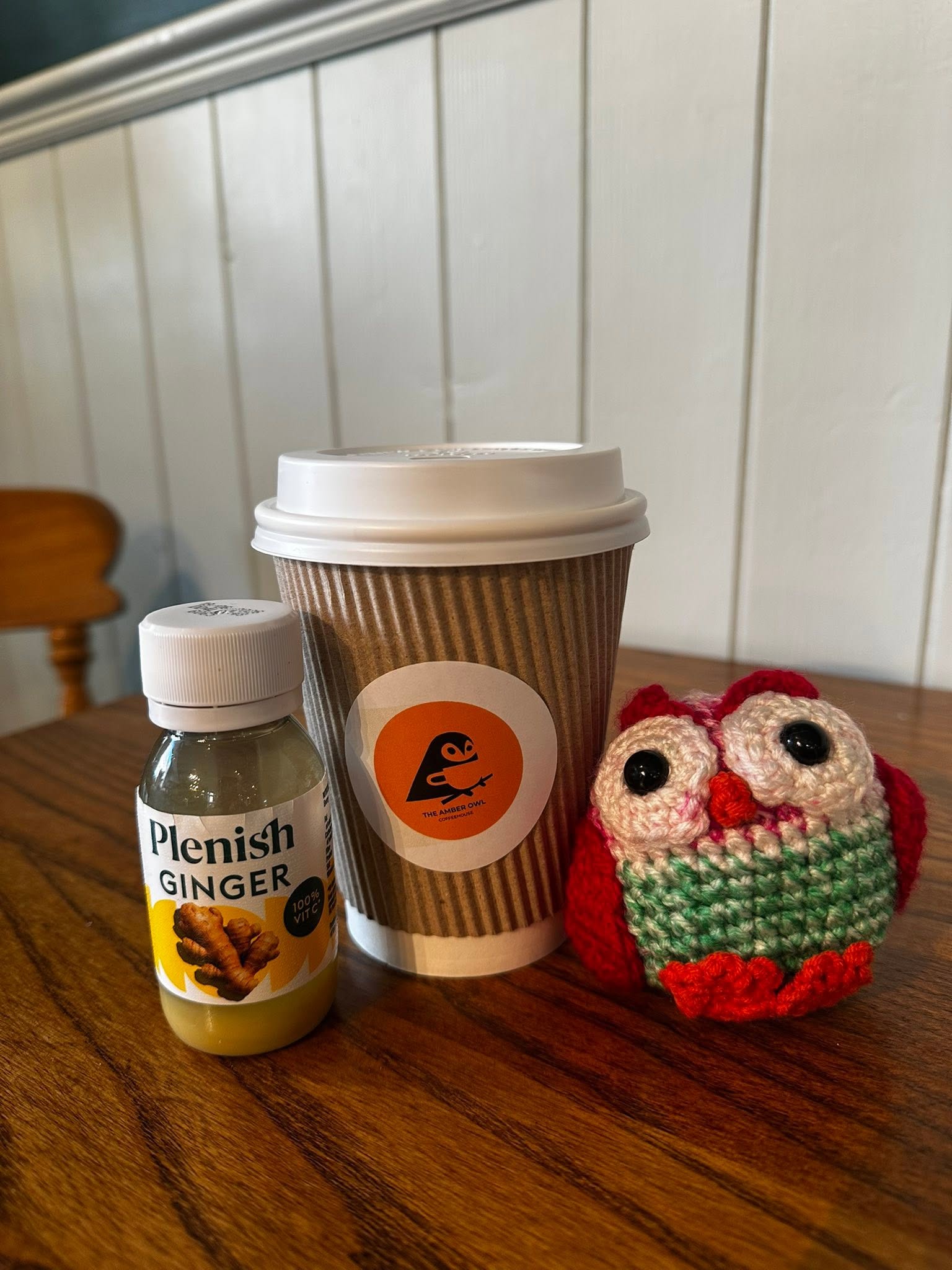 Takeaway coffee cup, a ginger shot, and the shop's crochet owl mascot