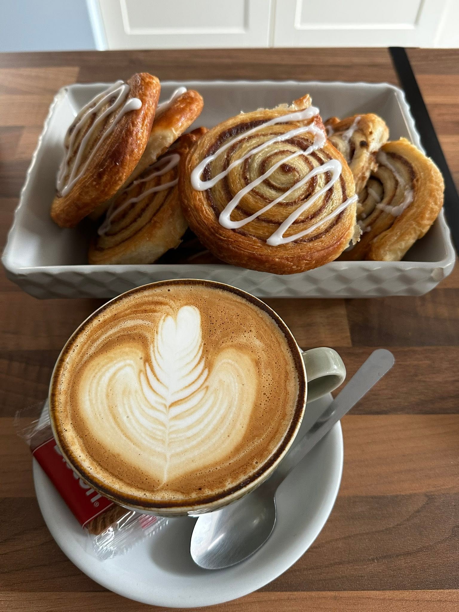 A basket of cinnamon pastries beside a cappuccino
