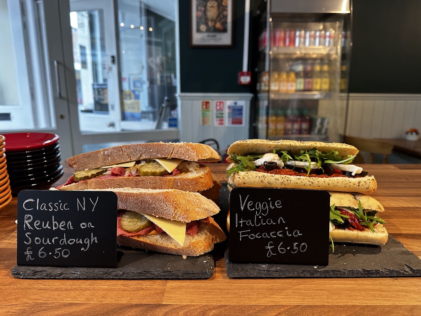 Sandwiches on the counter with handwritten chalkboard price signs