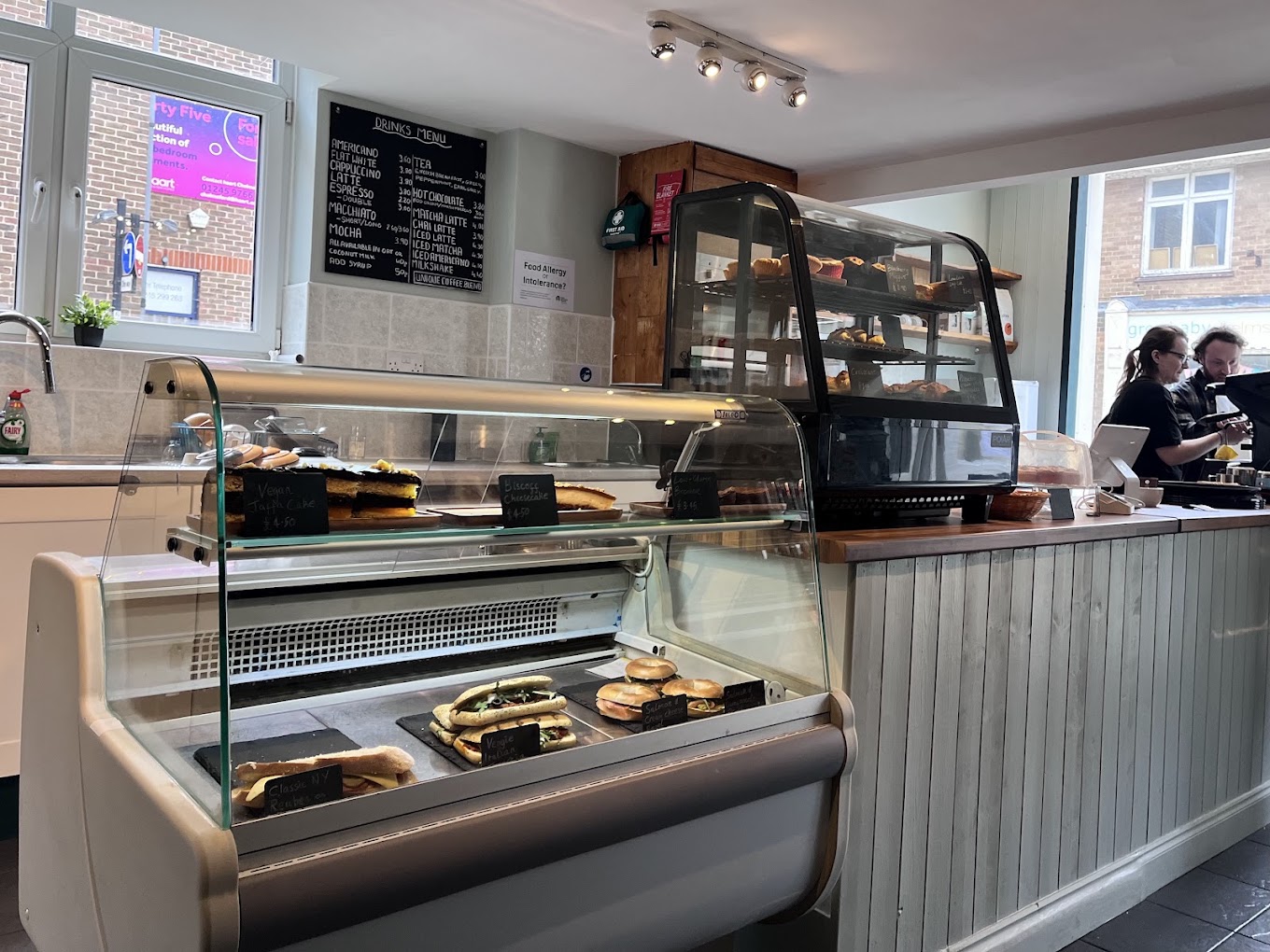 The counter and display cabinet, with cakes, bagels, and the drinks menu on the wall